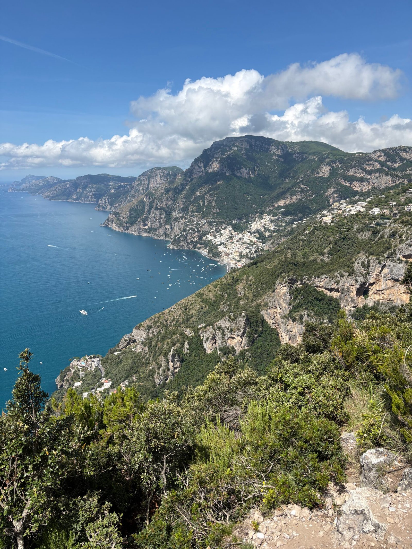 View of the Amalfi Coast from the Path of the Gods, with mountains, coastal towns and the hiking trail in the foreground.