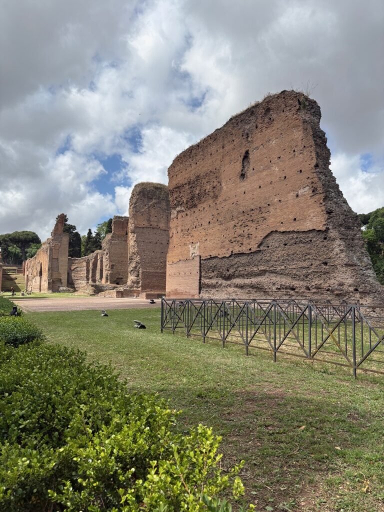Large brick ruins and green grounds at the Baths of Caracalla in Rome.