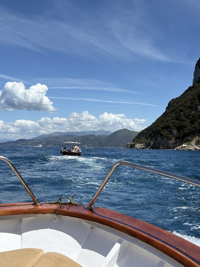 View over the bow of a boat leaving Capri, with the coastline ahead.