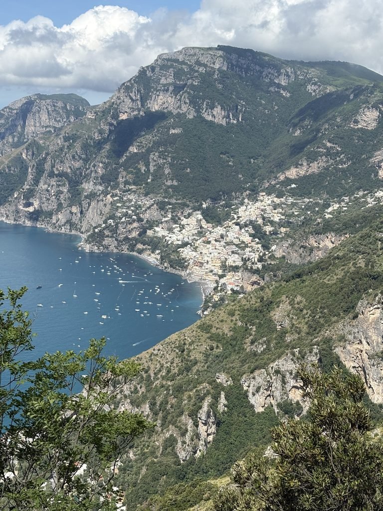 View of Positano and the Amalfi Coast from the Path of the Gods, with steep green mountains and the sea below.