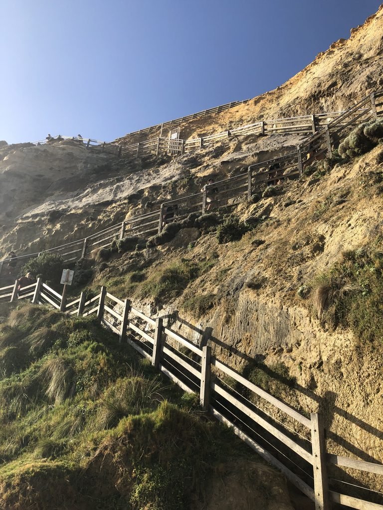 Long wooden staircase climbing a steep rocky coastal hillside.